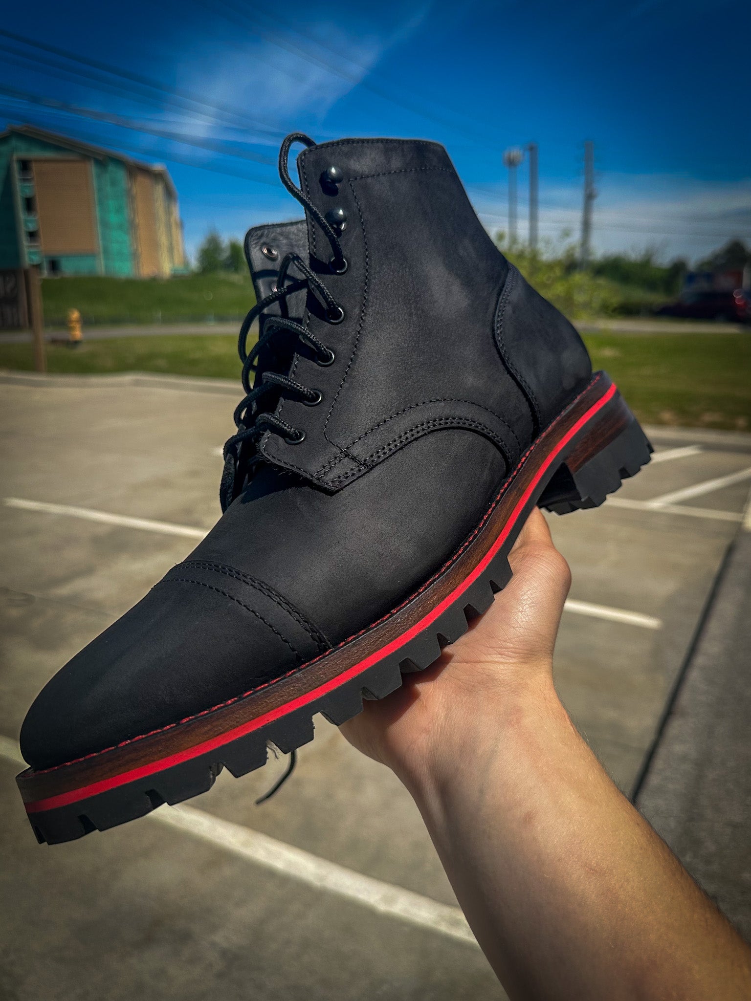 A pair of Black Matte Captain Thursday Boots after being customized with new Vibram 100 lug soles and heels with a red midsole and red stitching at the boot repair center 