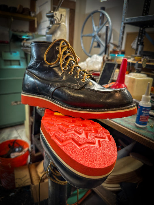 a pair of Redwing Moc-toe work boots after being repaired with new Red Vibram wedge soles at the Redwing Boot repair center