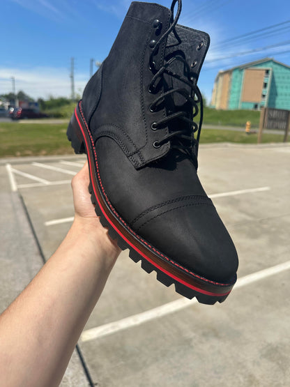 A pair of Black Matte Captain Thursday Boots customized with new Vibram 100 soles and heels with a red midsole and red stitching at the boot repair center