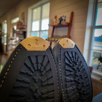 A close up of a pair of Thursday Boots after being repaired with Vibram 430 Mini Lug soles highlighting the Triumph Toe plates at the boot repair center 