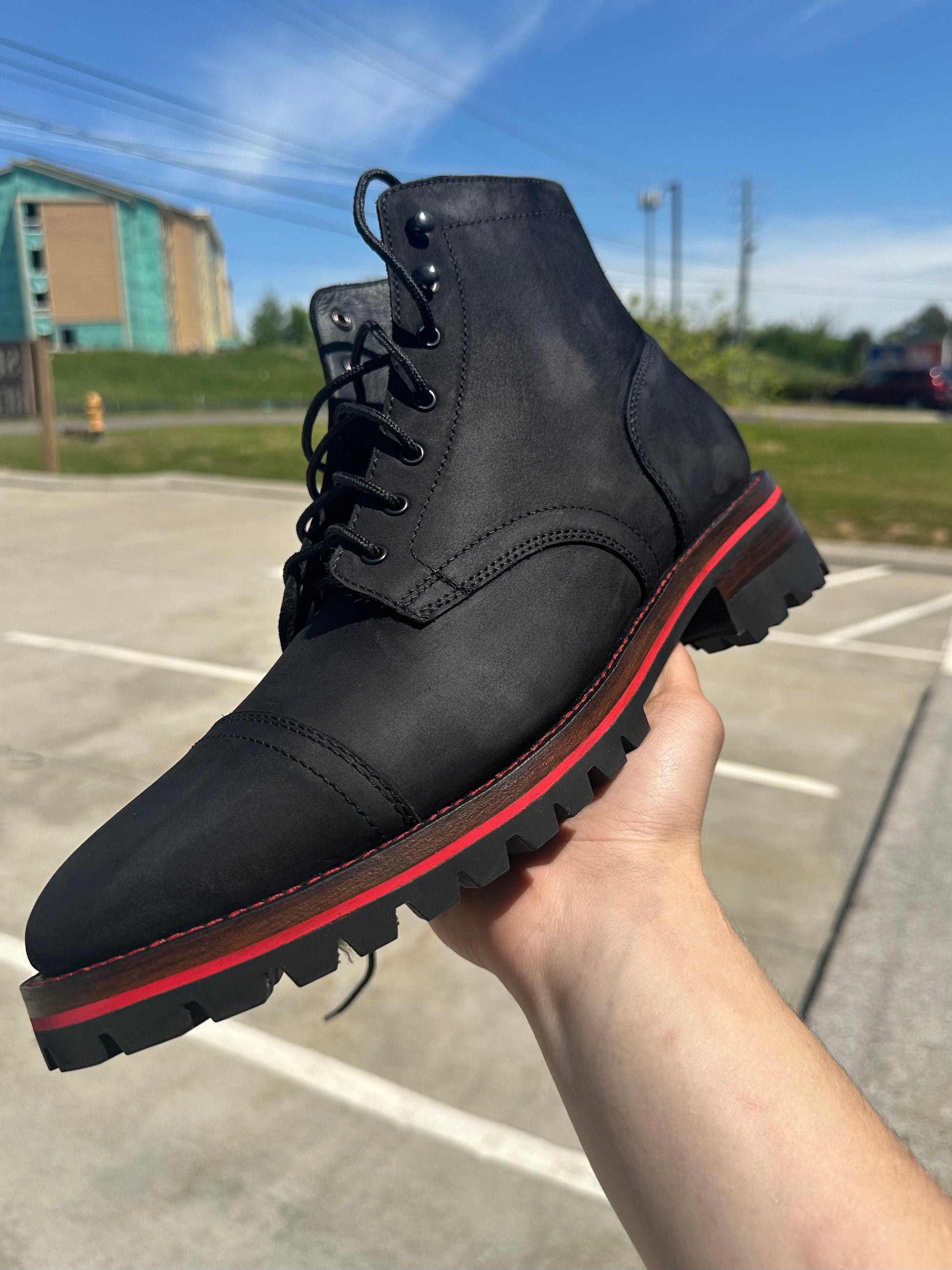 A pair of Black Matte Captain Thursday Boots customized with new Vibram 100 soles and heels with a red midsole and red stitching at the boot repair center