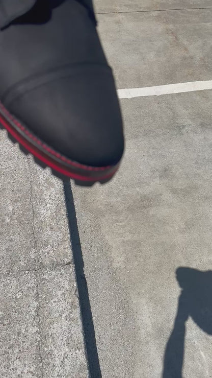 A pair of Black Matte Captain Thursday Boots customized with new Vibram 100 soles and heels with a red midsole and red stitching at the boot repair center.